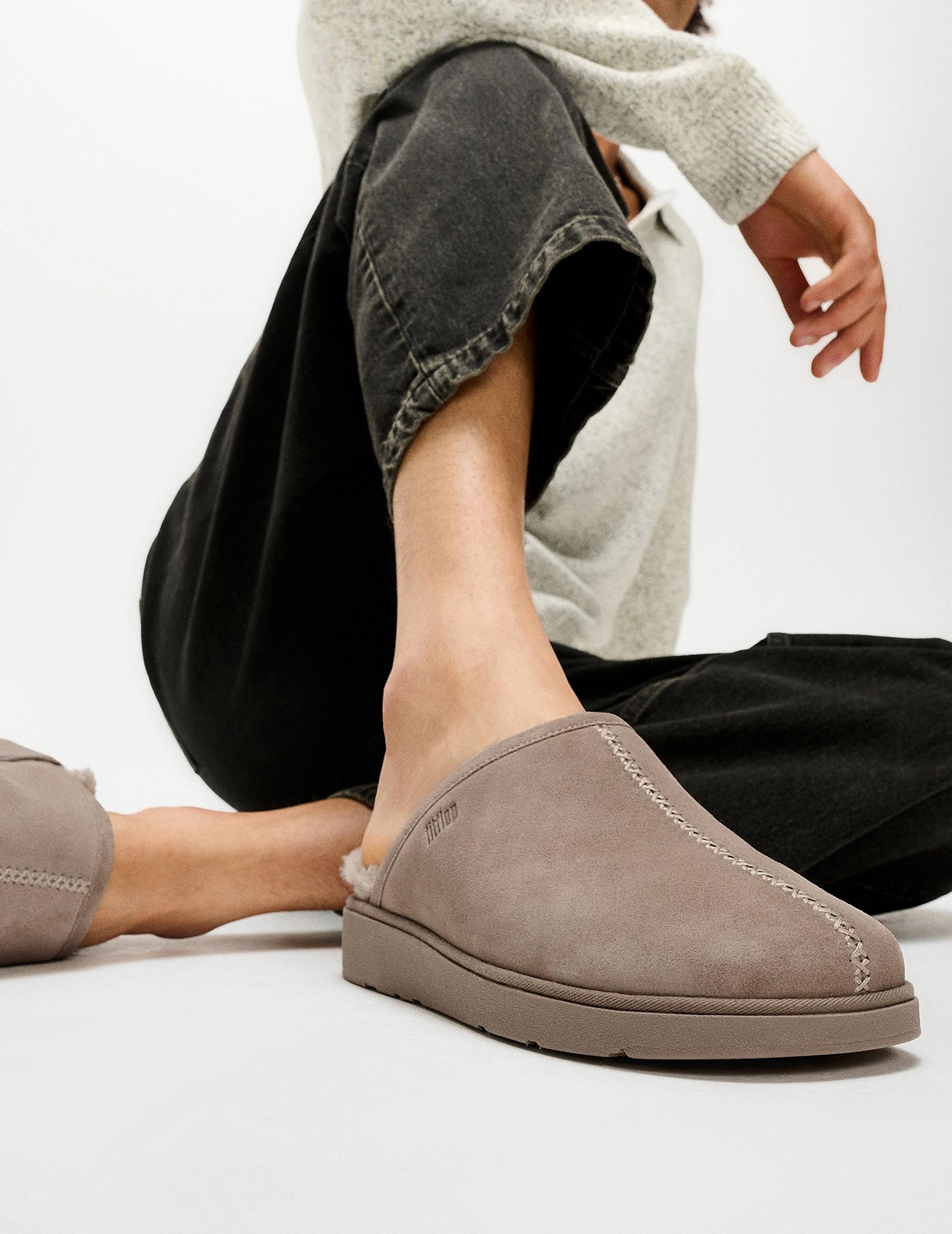 Close-up of taupe suede slip-on slippers with shearling lining, worn with black jeans and top