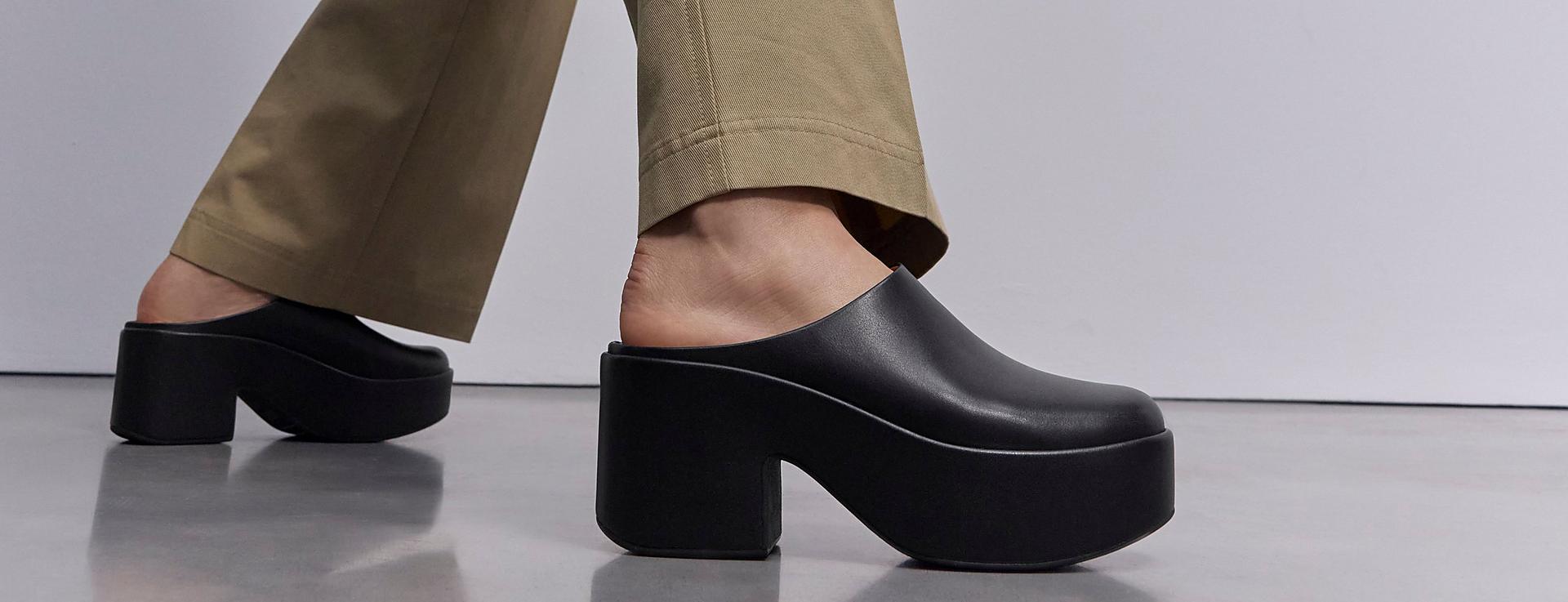 A female model wearing and styling black platform clogs.