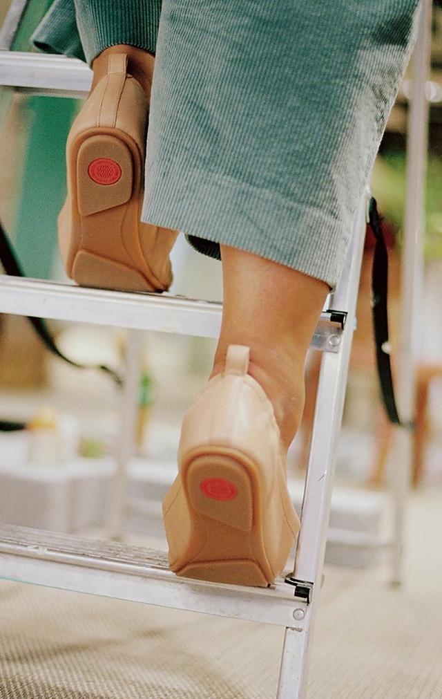 A woman is stepping up a ladder. She is wearing pale green suit trousers and ballerina shoes in a nude colour.