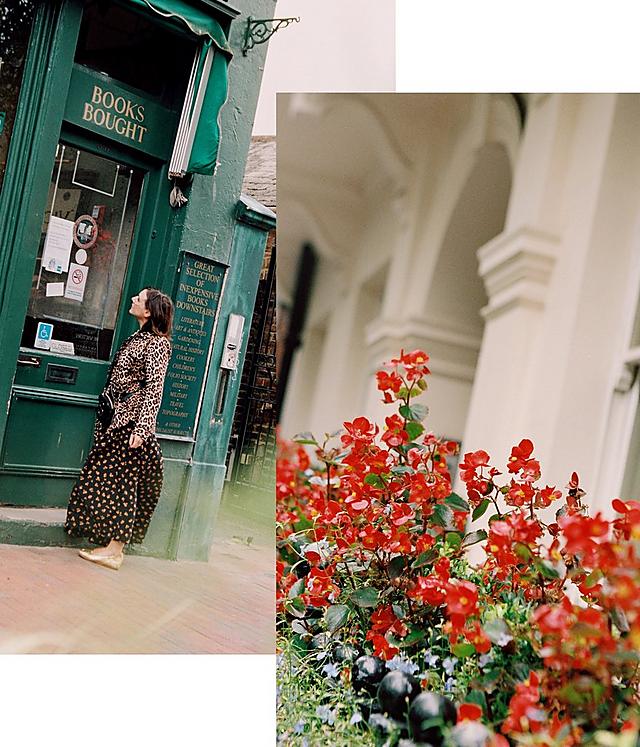 A woman wearing a black floral dress is looking into the window of a green book store. She is wearing ballerina shoes in gold.