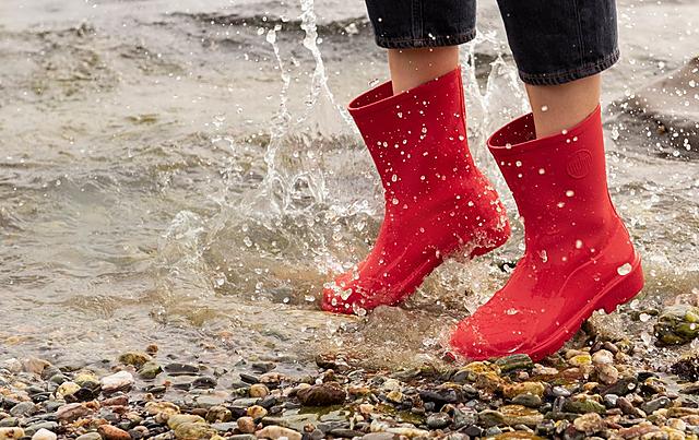Lady jumping in water wearing Fitflop red wellington boots.