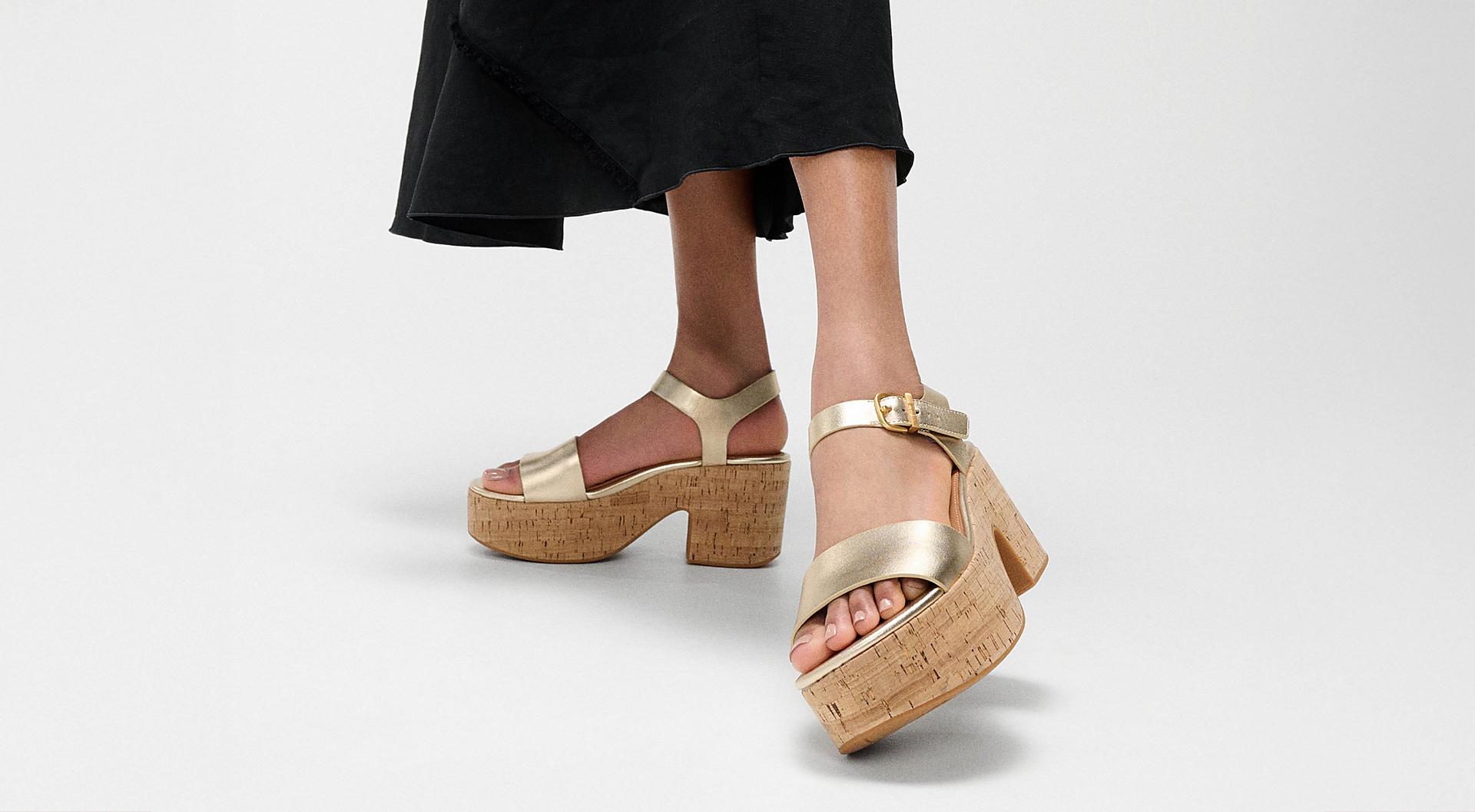 A female model wearing and styling a pair of platform sanadals in a gold metallic colour.