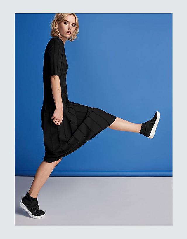 Women in black dress modelling Black slip-on high-top sneakers with white base.