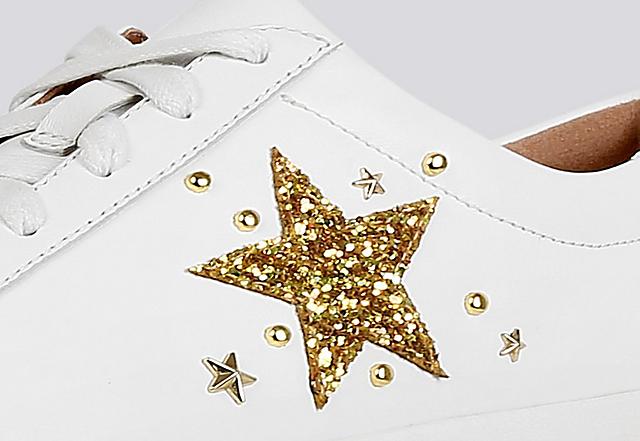 Close-up image of white leather Tennis style sneakers with gold embellished star print on the side.