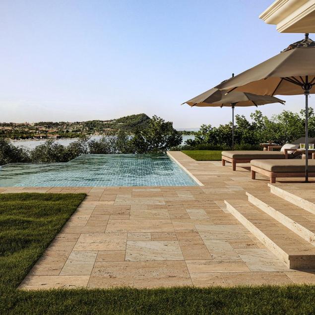 A travertine pool deck with chairs and umbrellas.