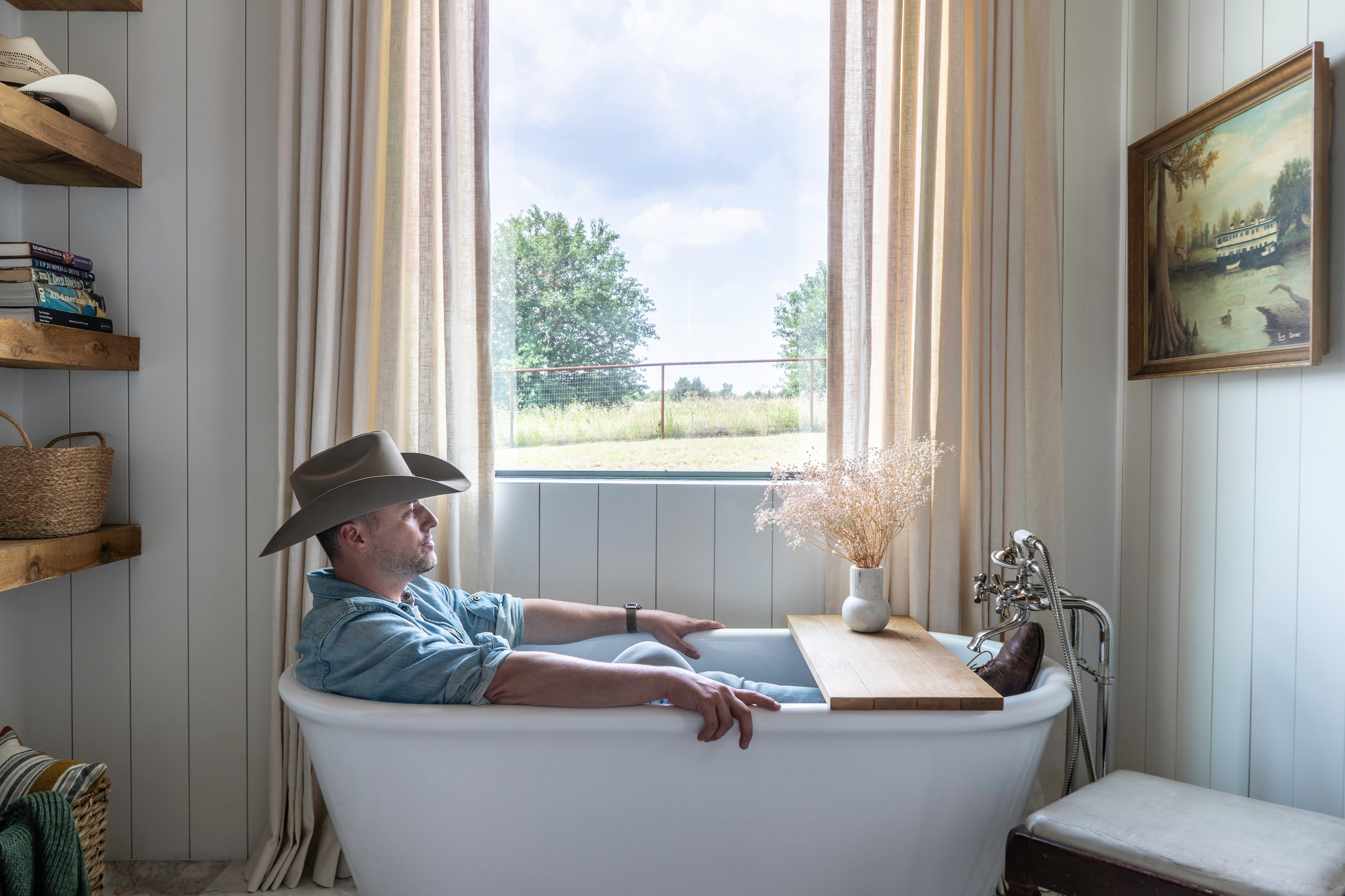 Man with cowboy hat sitting in bathtub.