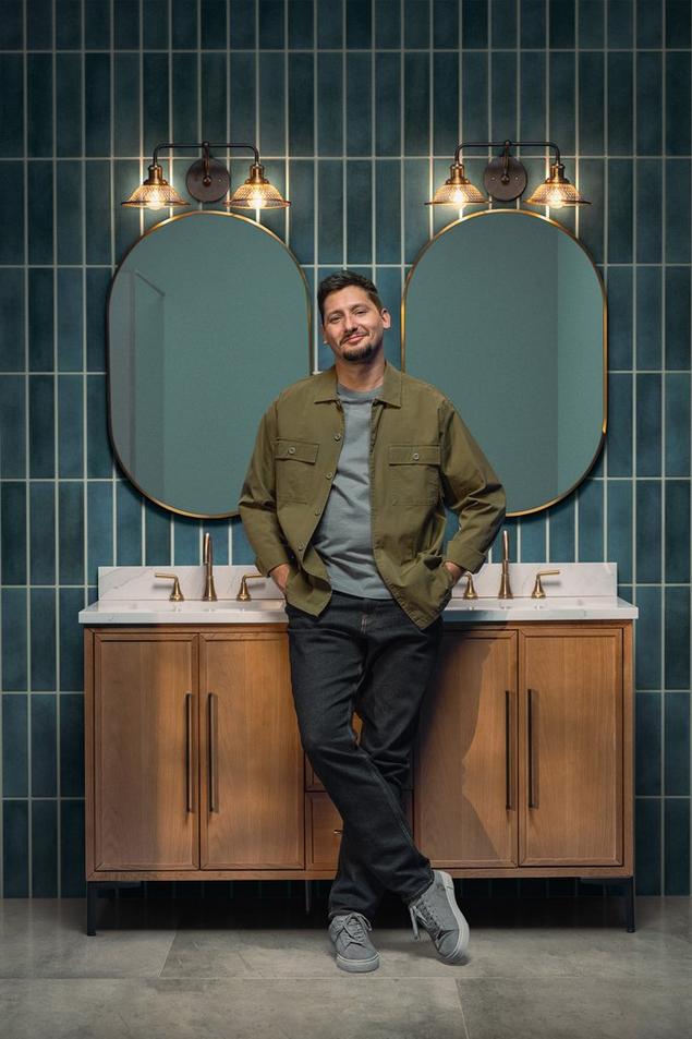 Man posing against vanity in bathroom with blue stacked backsplash tile.