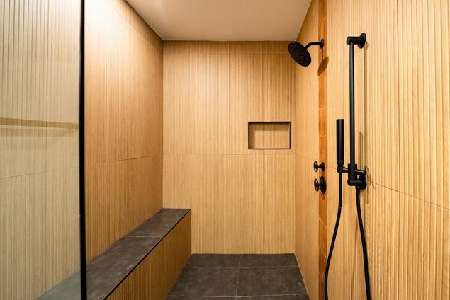 Shower with wood-look matte tile walls and black tile flooring.