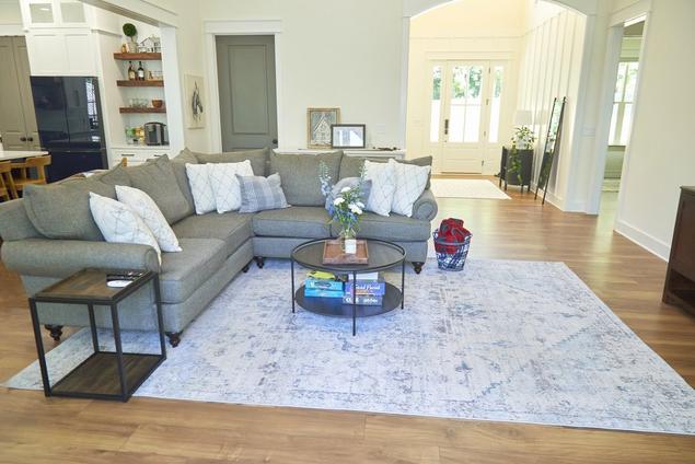 Shannon's white living room with light-medium brown wood-look flooring and gray l-shaped couch.