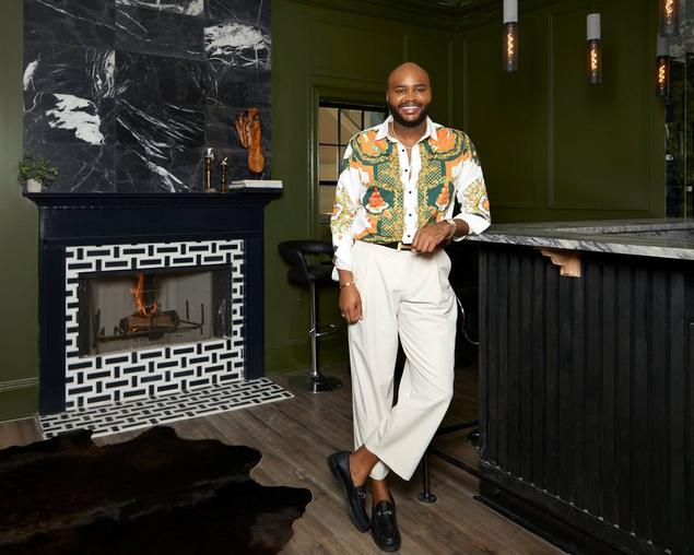 Ron posing next to his terrace bar, mirror wall tile and black and white fireplace seen behind him.