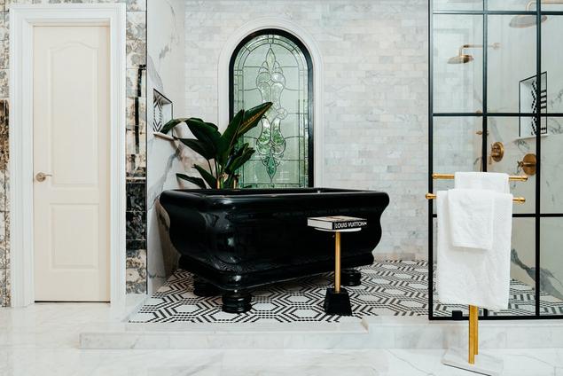 Bathroom with custom black bathtub, black and white mosaic floors, and white marble shower walls.