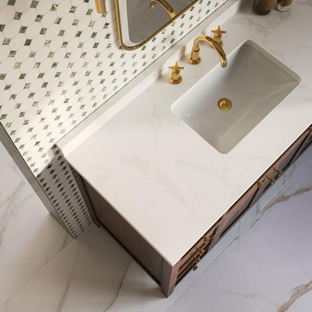 Overhead bathroom view of white vanity top, gold faucet hardware, and white and green marble mosaic.