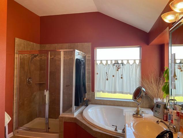 Before image of the bathroom with red walls, corner bathtub with window, and separate glass shower.