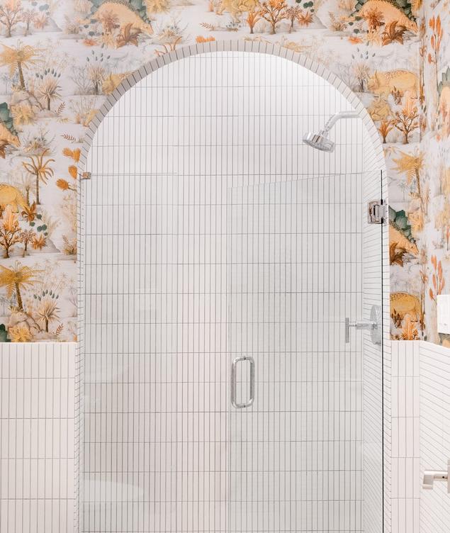 Playful arched shower with white stacked mosaic tile and dinosaur wallpaper.