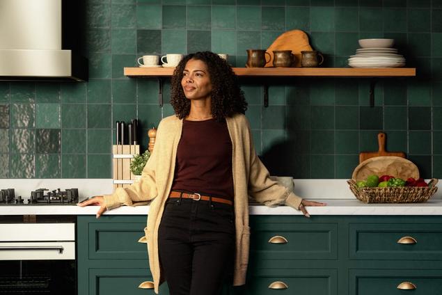 Woman smiling in kitchen with green backsplash tile visible behind her.