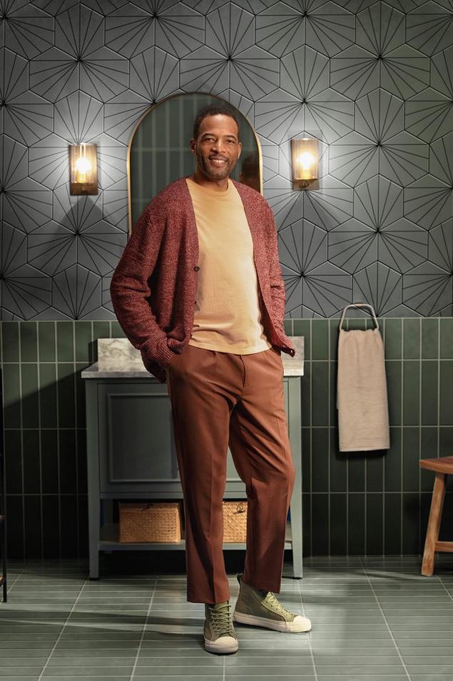 Man in bathroom with black and white hexagon and green stacked backsplash tile.