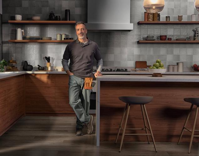 Man in kitchen with white zellige backsplash tile and engineered hardwood.