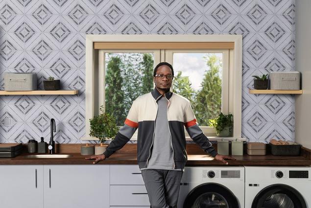 Man in laundry room with black and white motif wall tile and butcherblock countertop.