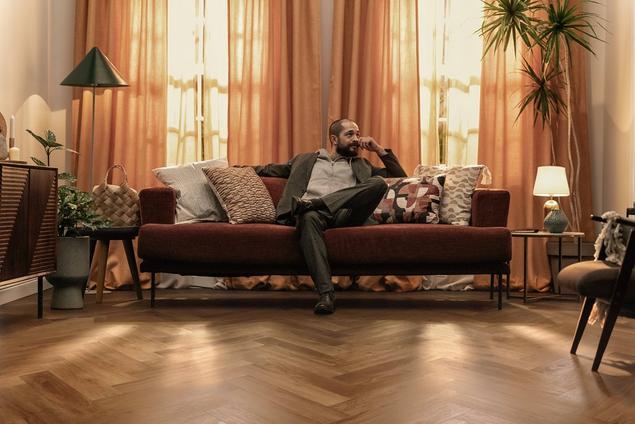 Man sitting in living room with medium-brown luxury vinyl plank floors.