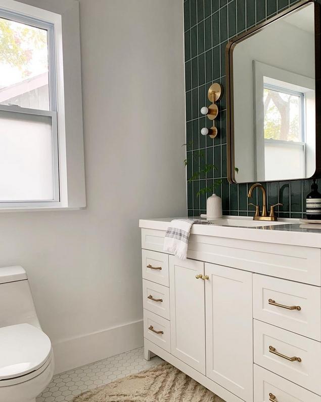 Half bath with white hexagon tile floors, green tile backsplash & white vanity with bronze hardware.