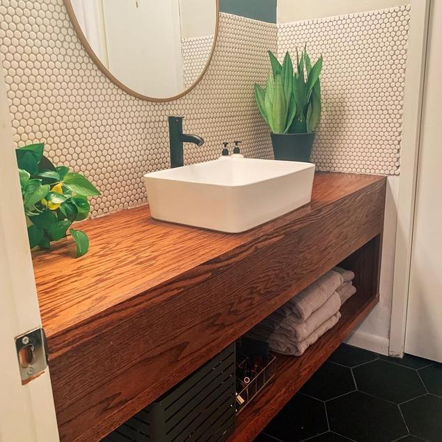 A woodgrain bathroom vanity sits beneath a backsplash made of a white porcelain penny tile mosaic.