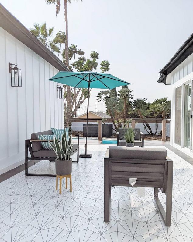 An attractive outdoor patio area with a tiled floor and beach umbrella. 