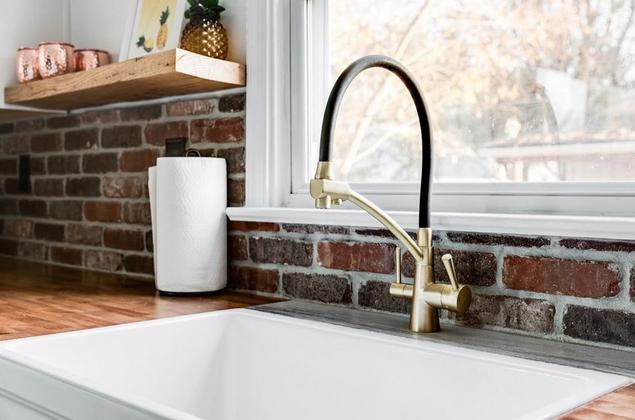 A white sink with brass faucets and brick backsplash.