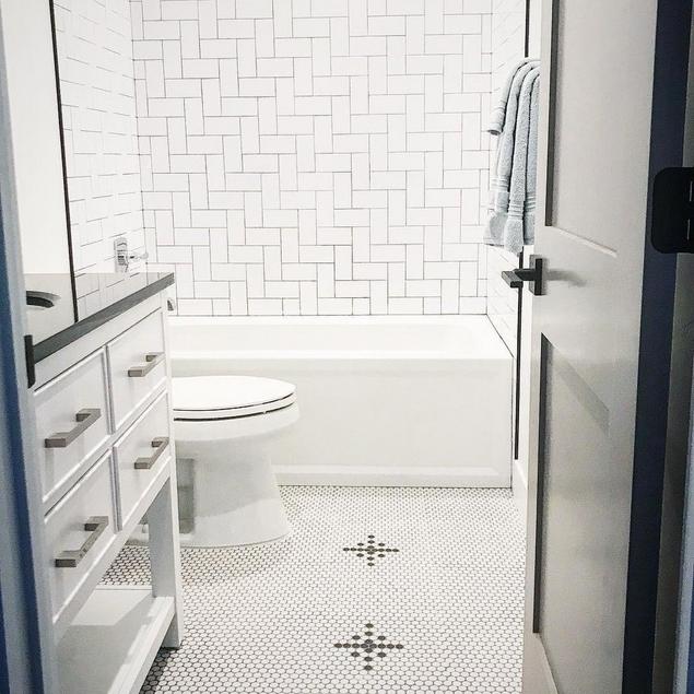 A white bathroom with white penny tile flooring, decorated with a black diamond design.