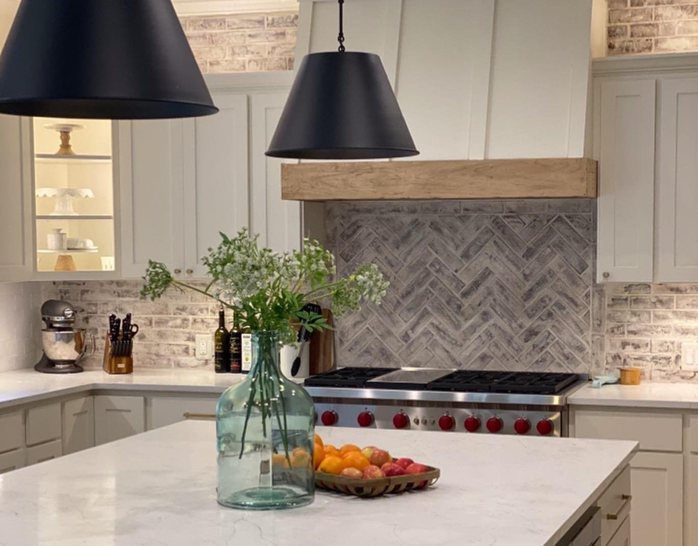 A kitchen with marble countertops and herringbone backsplash.