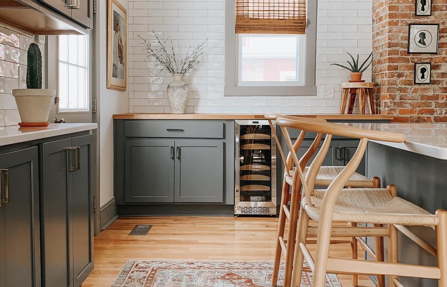 A kitchen with white brick walls, grey cabinets, and hardwood flooring.