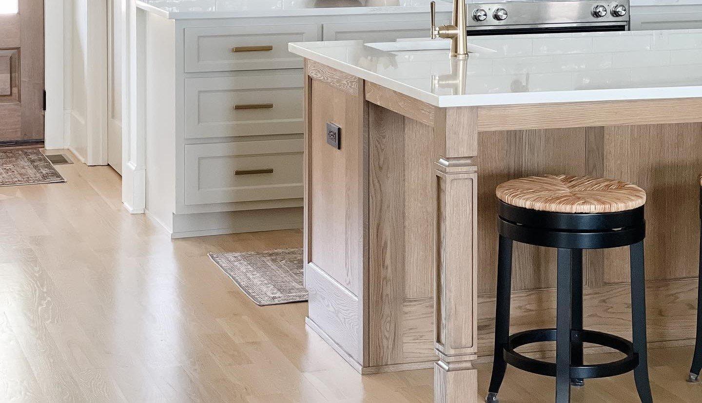 A kitchen with white backsplash and white cabinets and light hardwood.