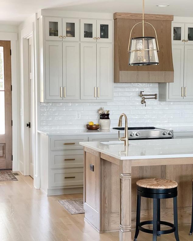 Kitchen with white backsplash tile, wooden island, white countertops and cabinets with gold hardware