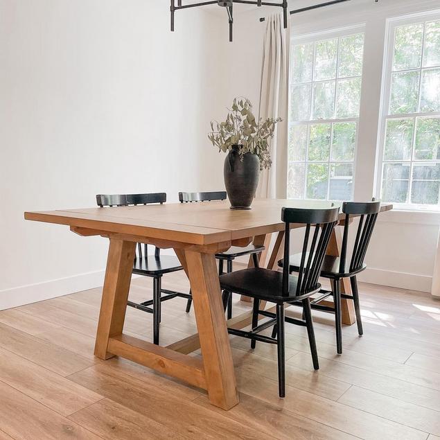 A dining room with large windows, blond wood-look floors, and a four-seater table.