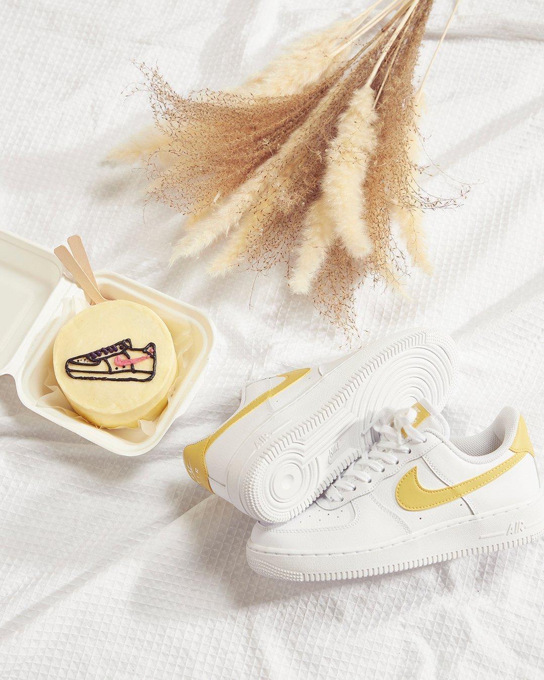 Nike Air Force 1 in Weiß mit gelben Swoosh neben Kuchen mit Sneaker Dekoration