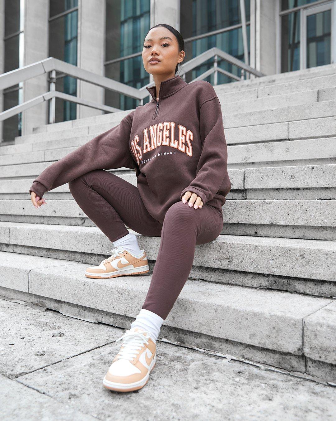 Frau in braunem Trainingsanzug von Supply & Demand und Air Force 1 Sneakern