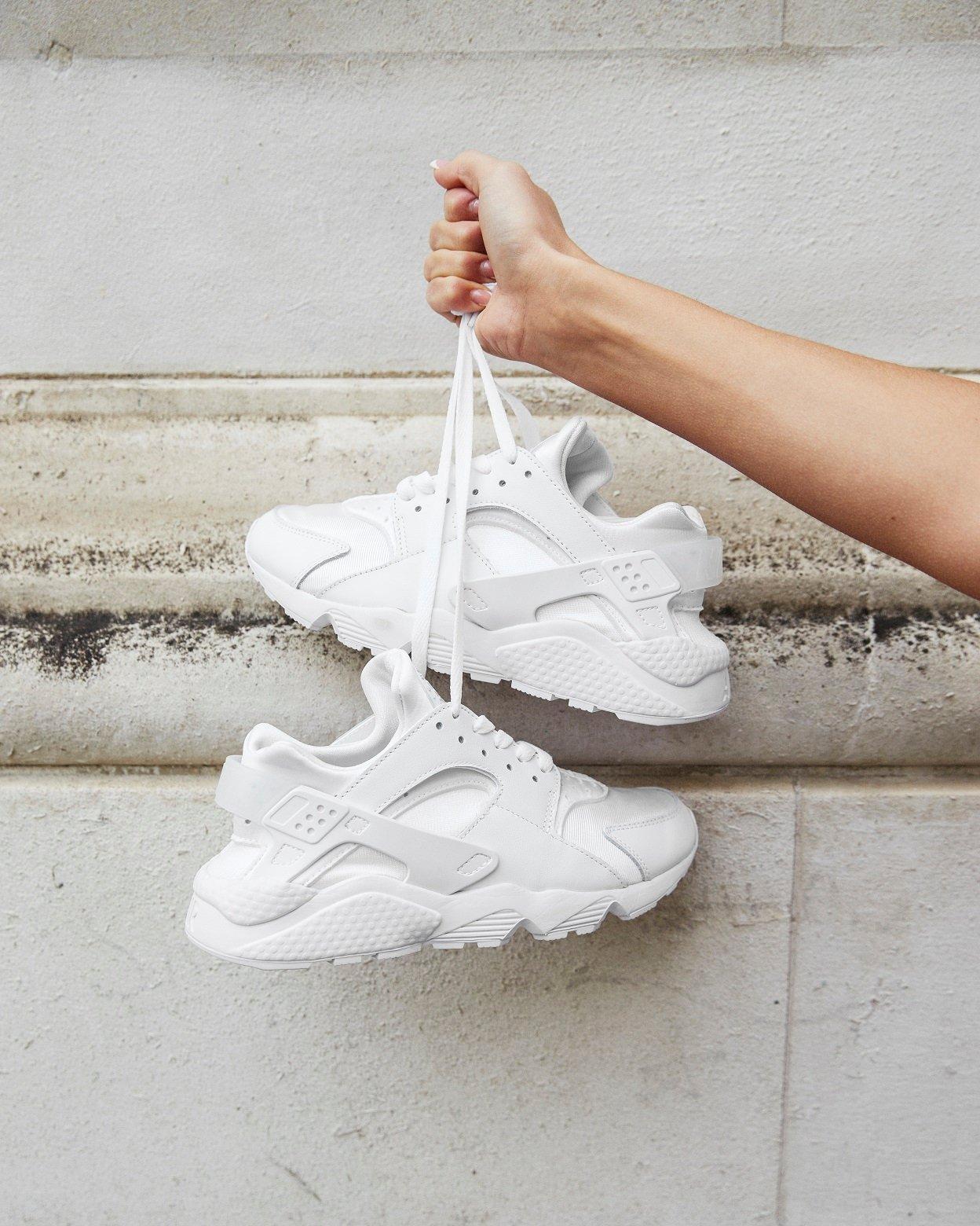 Nike Air Huarache in Weiß, hochgehalten an Schnürsenkeln