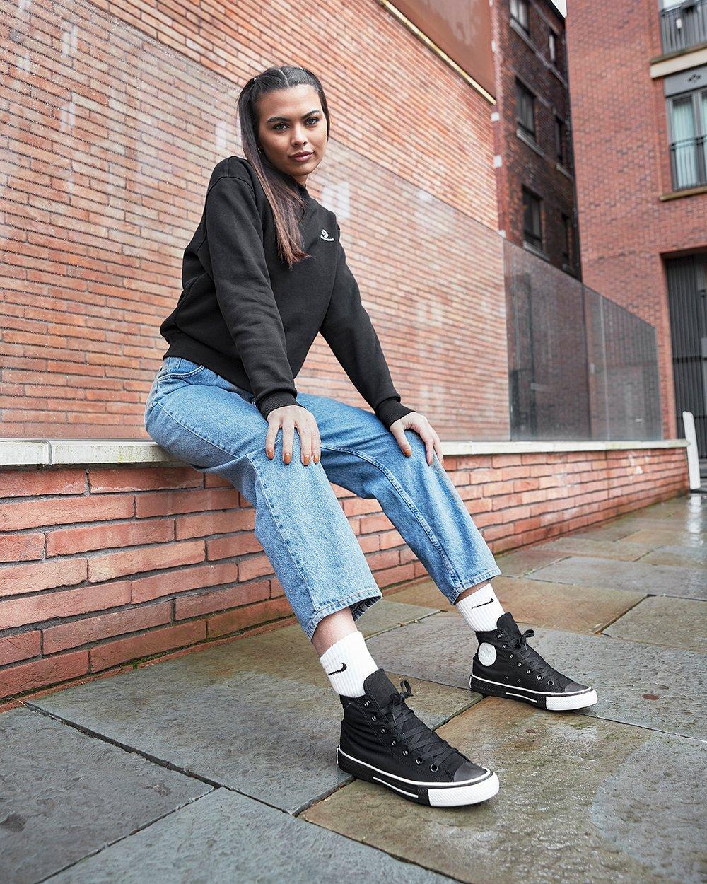 Outfit de mujer con sudadera Converse, pantalones vaqueros y zapatillas negras Converse All Star High con calcetines blancos Nike