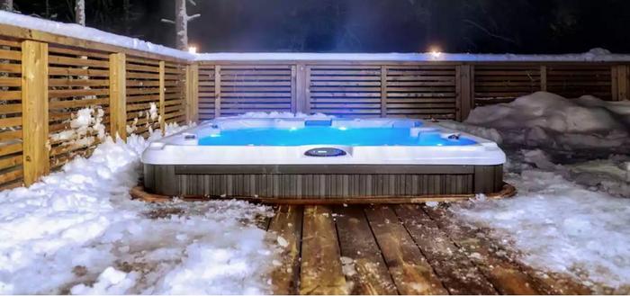 hot tub on a deck surrounded by snow with steam rising from the water
