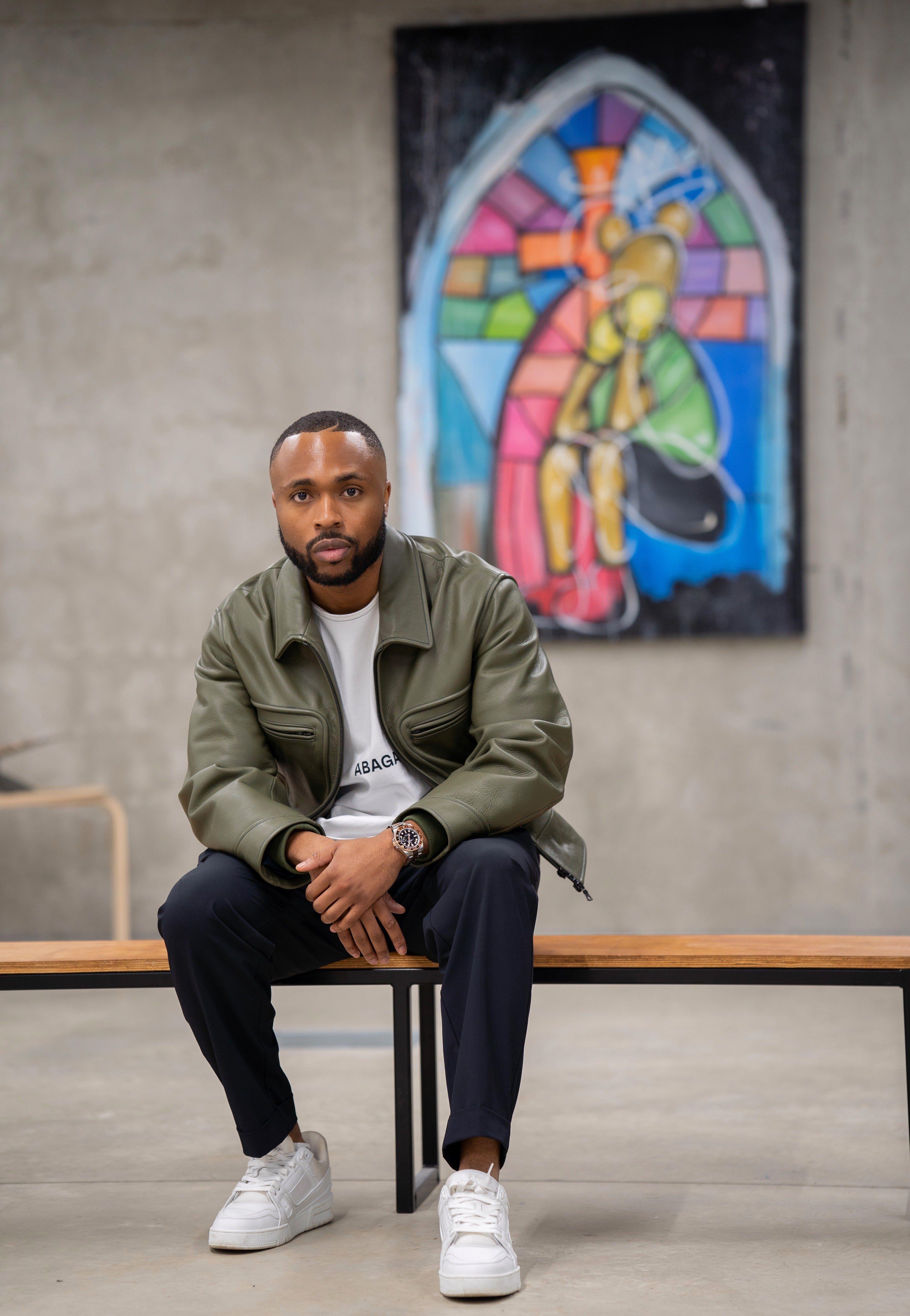 Feyi Badejo sits in front of his artwork