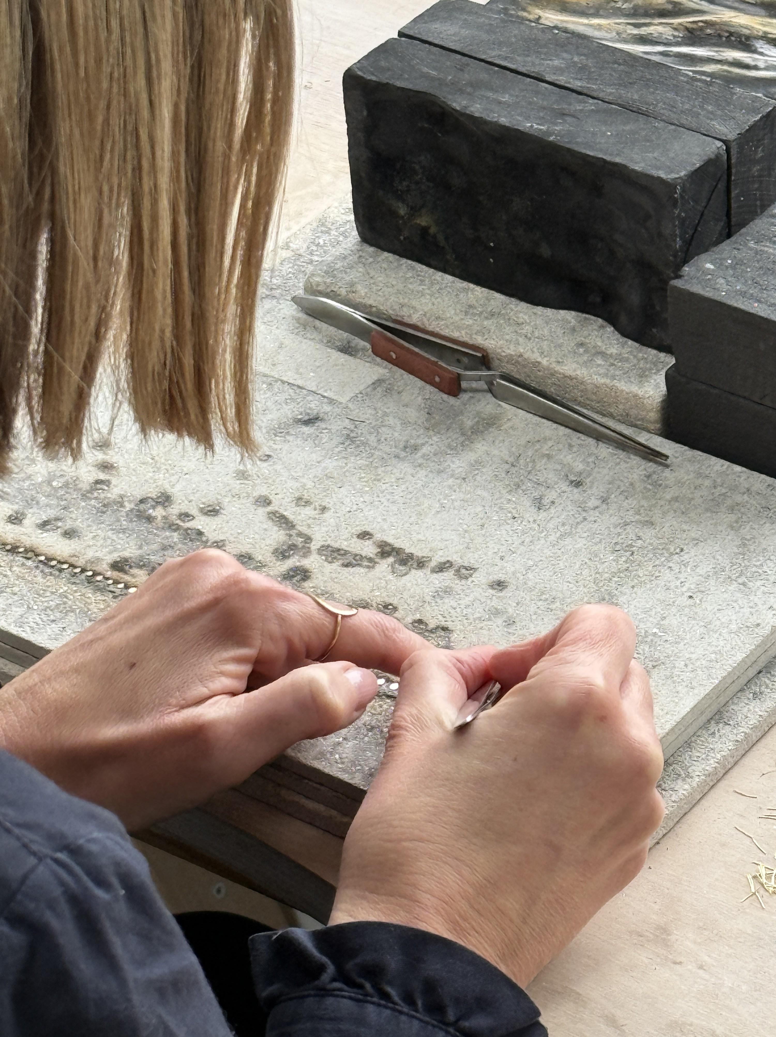 Jewellery designer Sia Taylor stands at a desk wearing a black blazer and her own necklace design