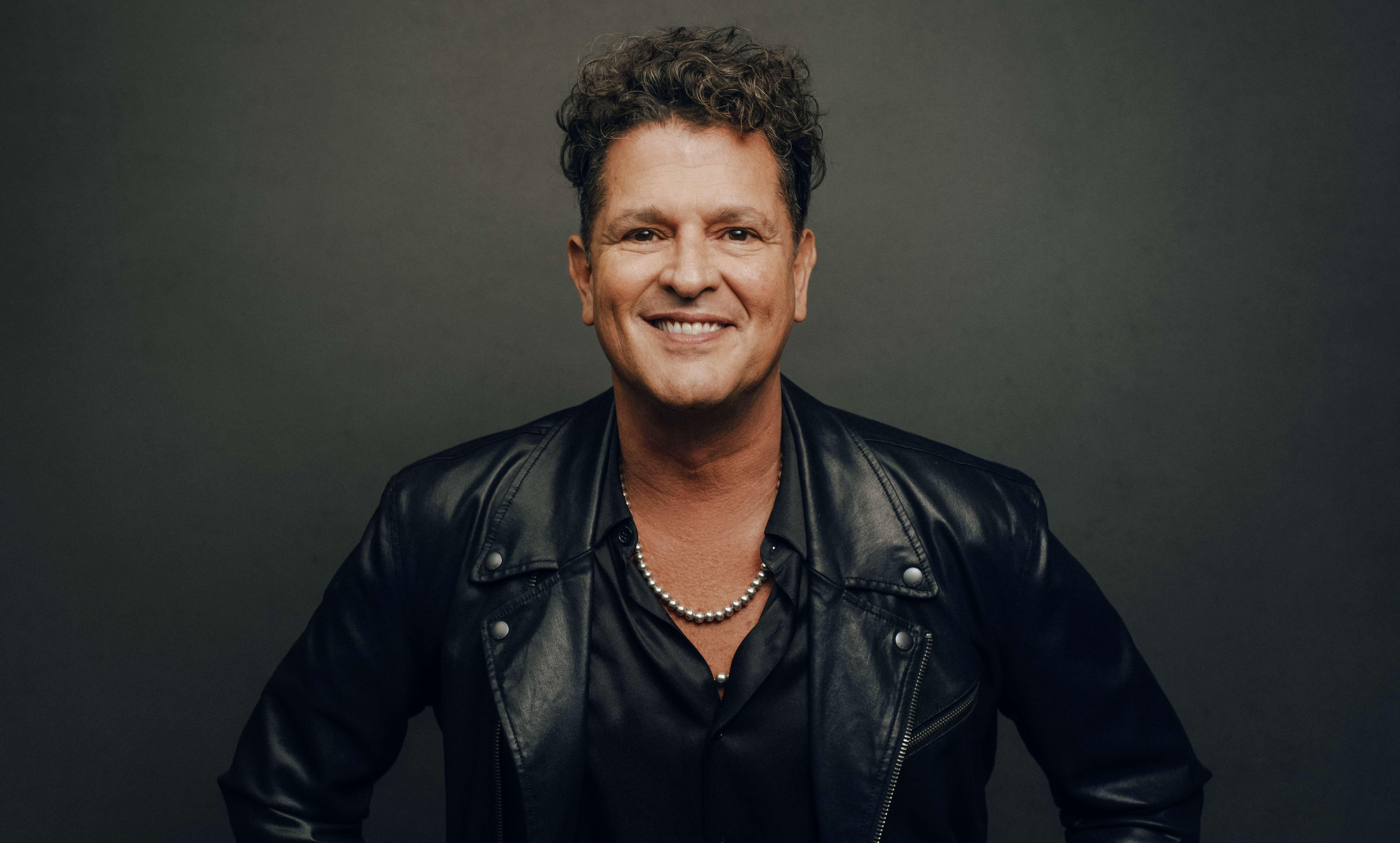 Photo of Carlos Vives wearing a black shirt, black leather jacket and a silver necklace.