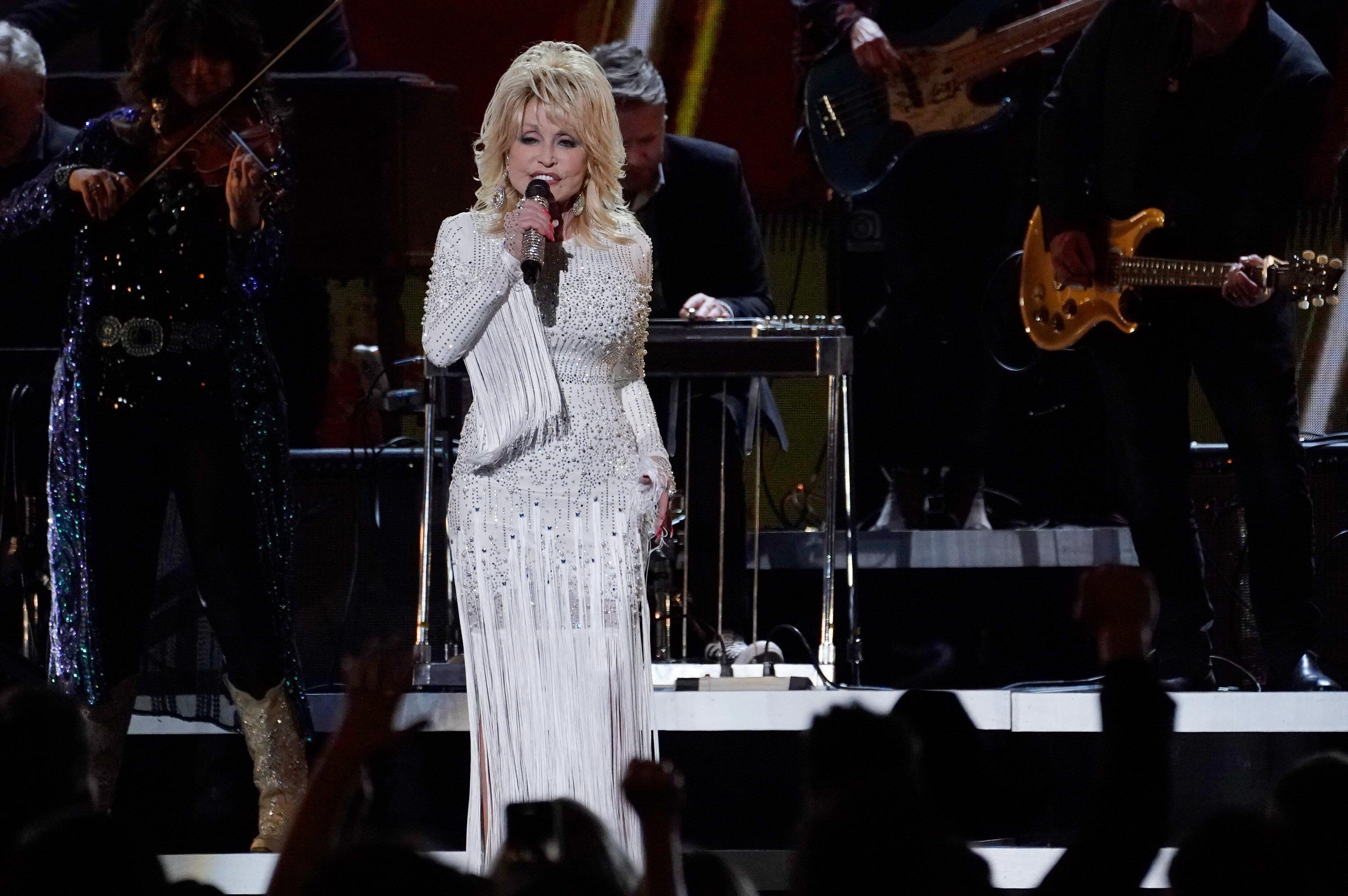 Dolly Parton sings on stage in a white fringed dress