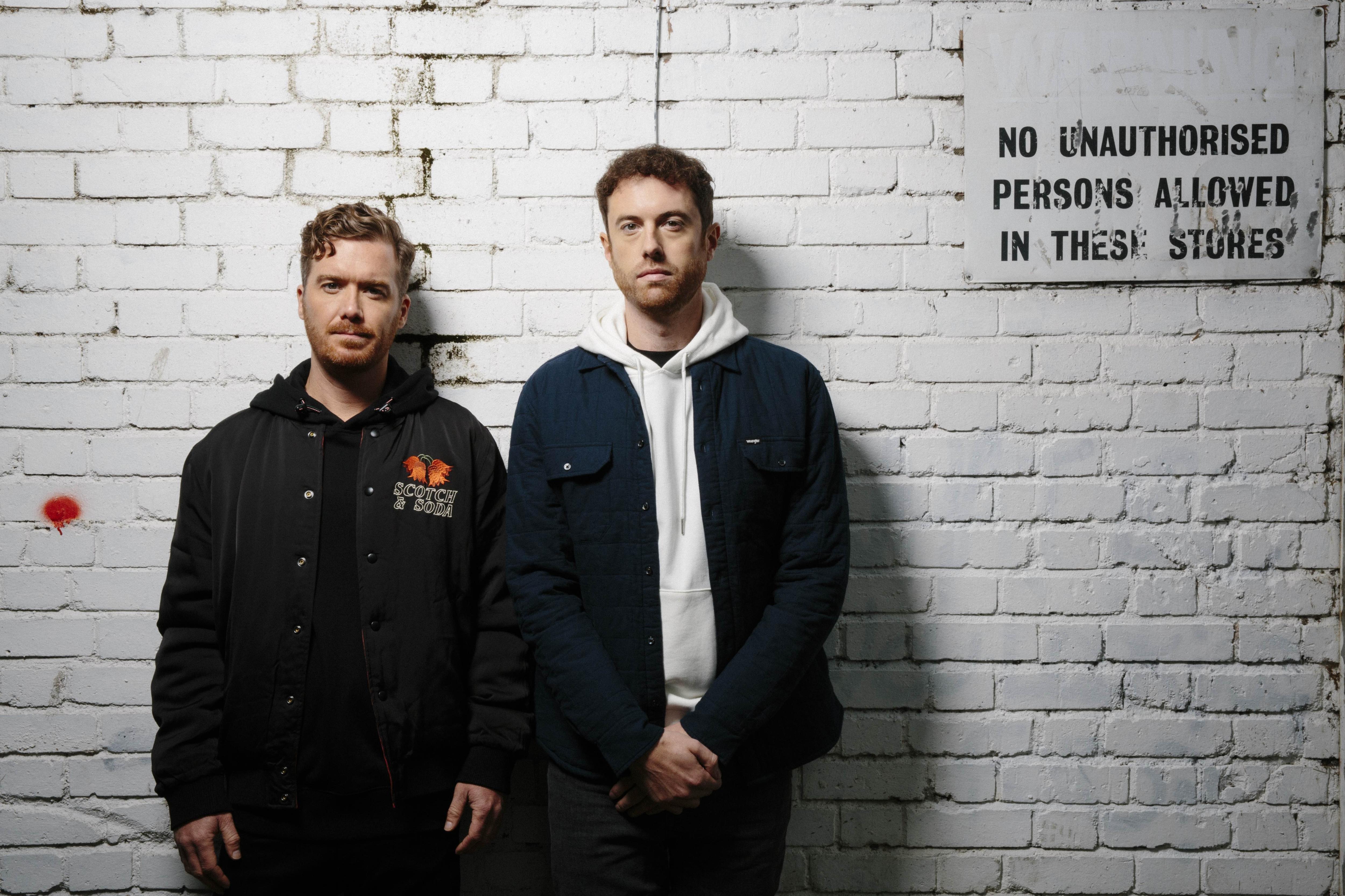 DJ/producer duo Gorgon City pose in front of a white brick wall