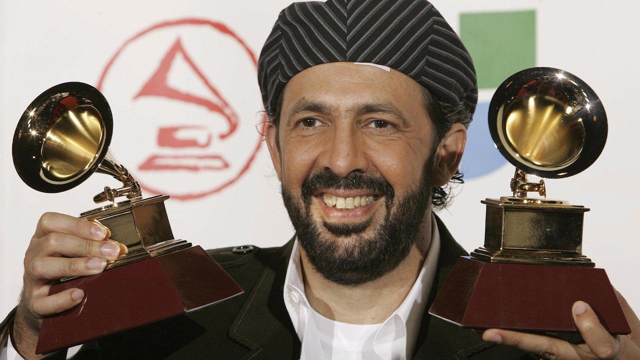 Juan Luis Guerra smiles and holds up two Latin GRAMMYs