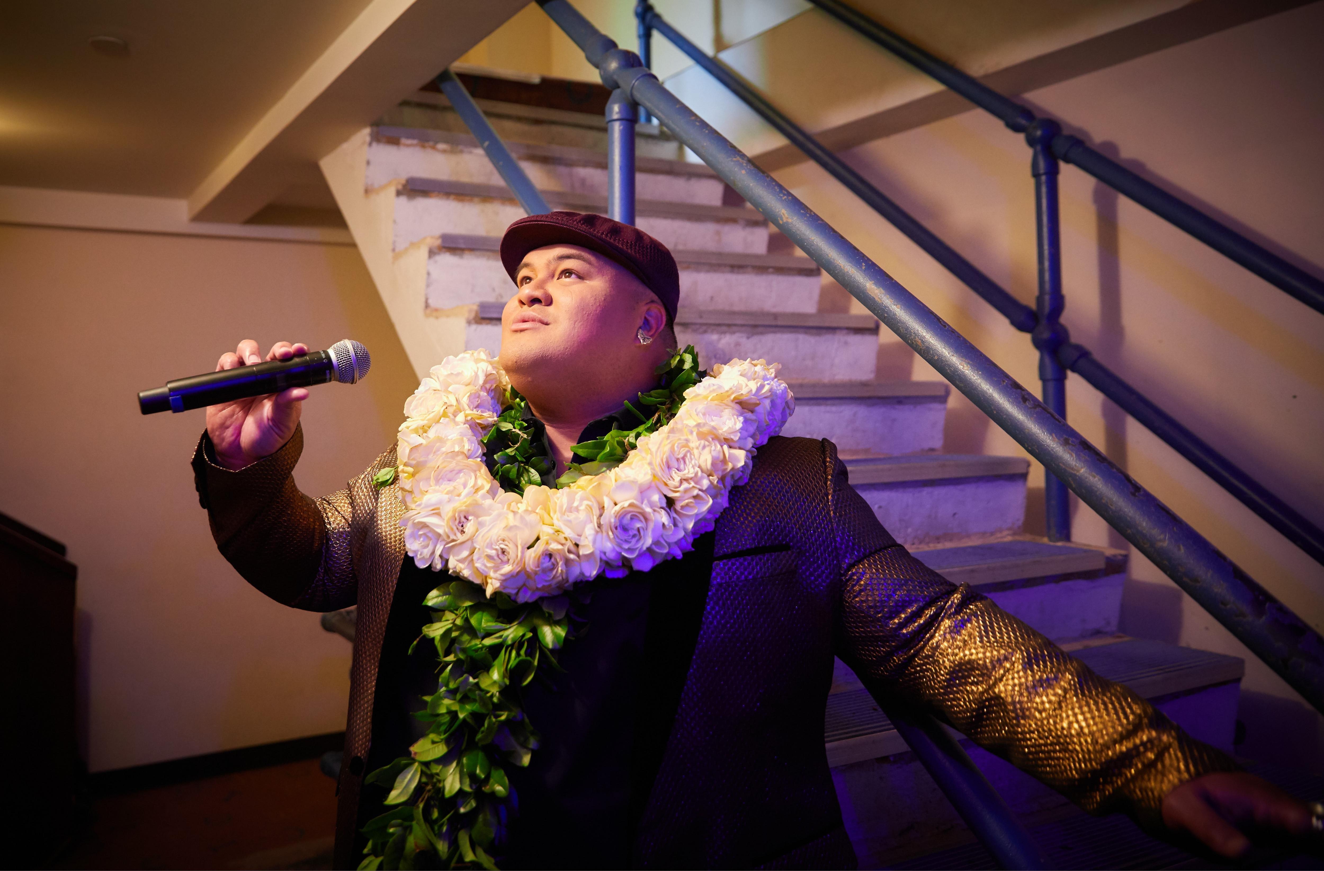 Kalani Pe'a looks up as he sings with a white rose lei