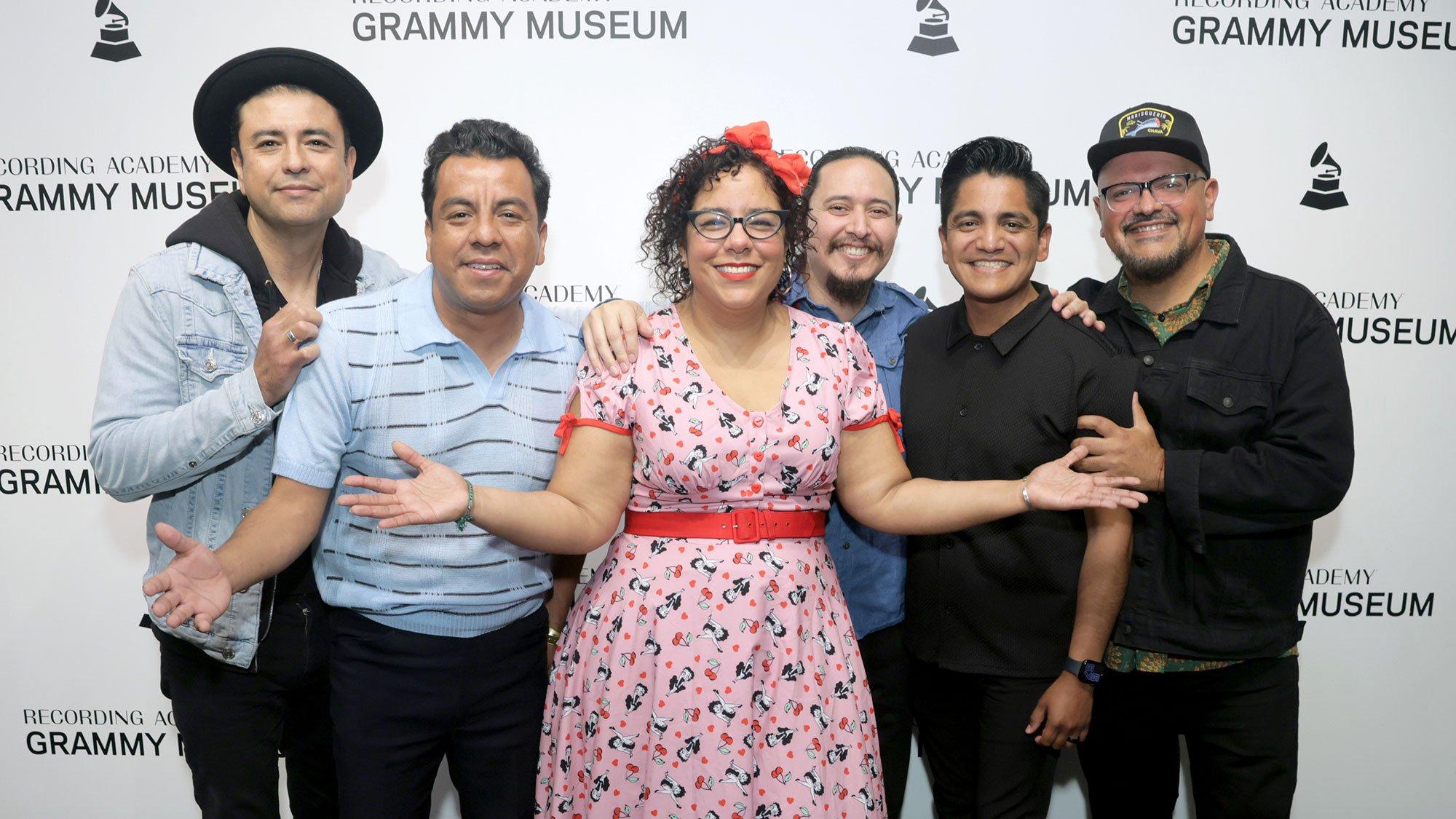 La Santa Cecilia poses for a photo together in front of a step and repeat at the GRAMMY Museum