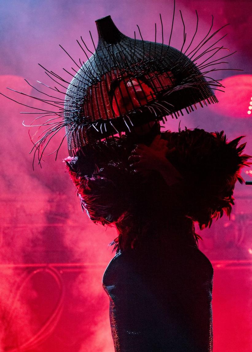 Lady Gaga występuje na Grammy 2026. Stoi na scenie przed mikrofonem, ubrana w kask w kształcie klatki dla ptaków i prostą, czarno-czerwoną sukienkę.