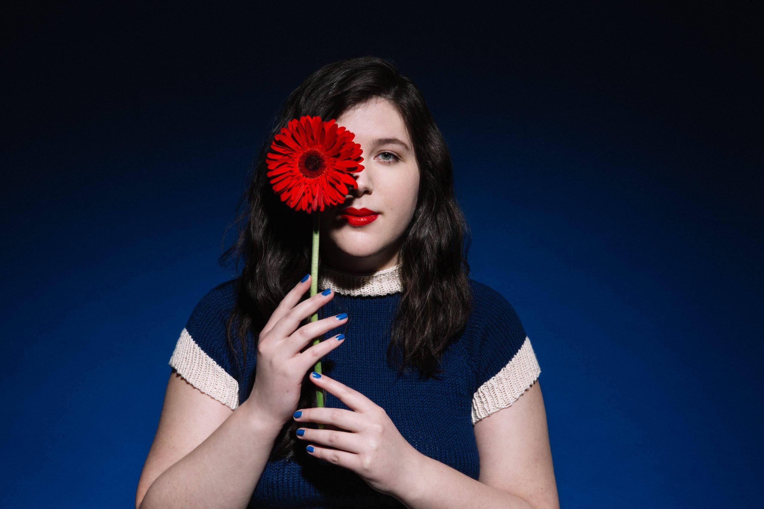 Lucy Dacus poses with a red flower over one eye 