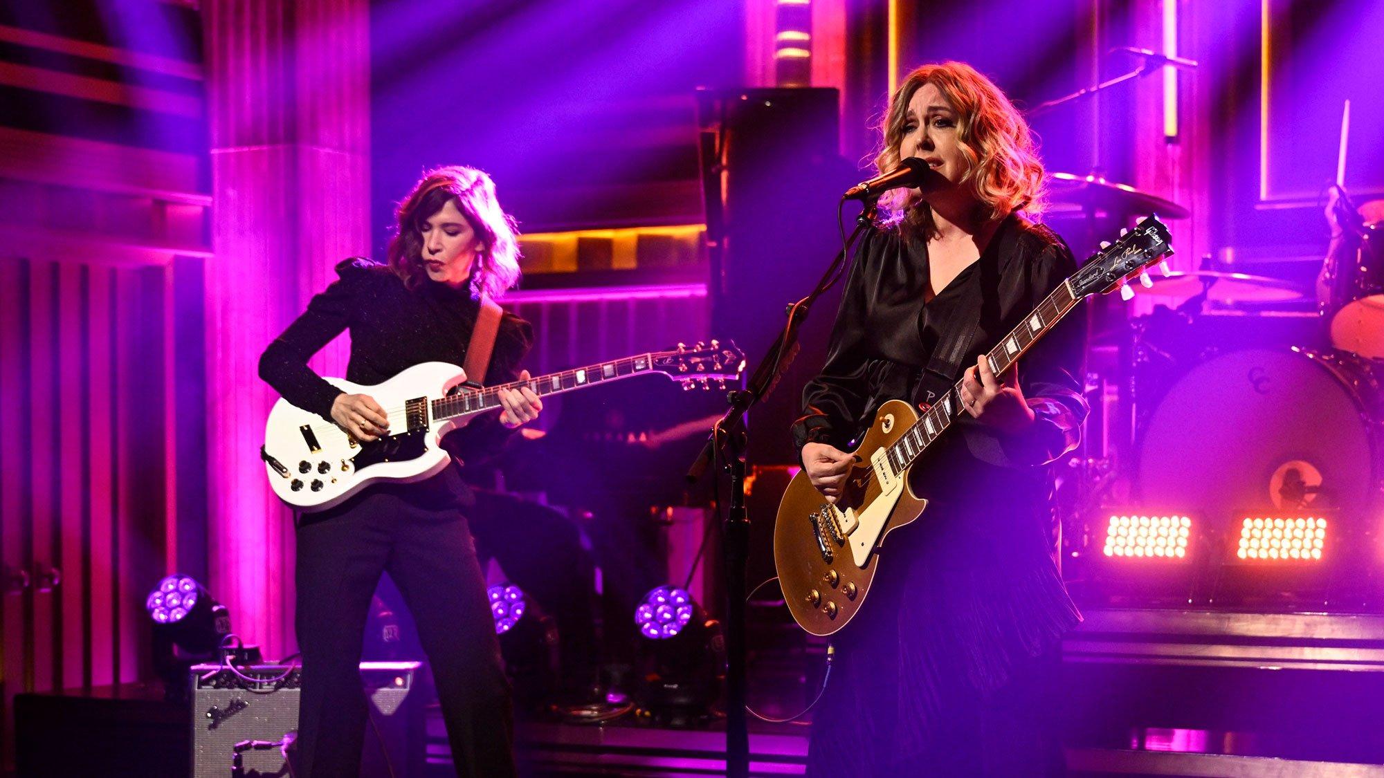 Sleater-Kinney's Carrie Brownstein and Corin Tucker play instruments and sing under red lights during a performance on the set of the Jimmy Fallon Show.