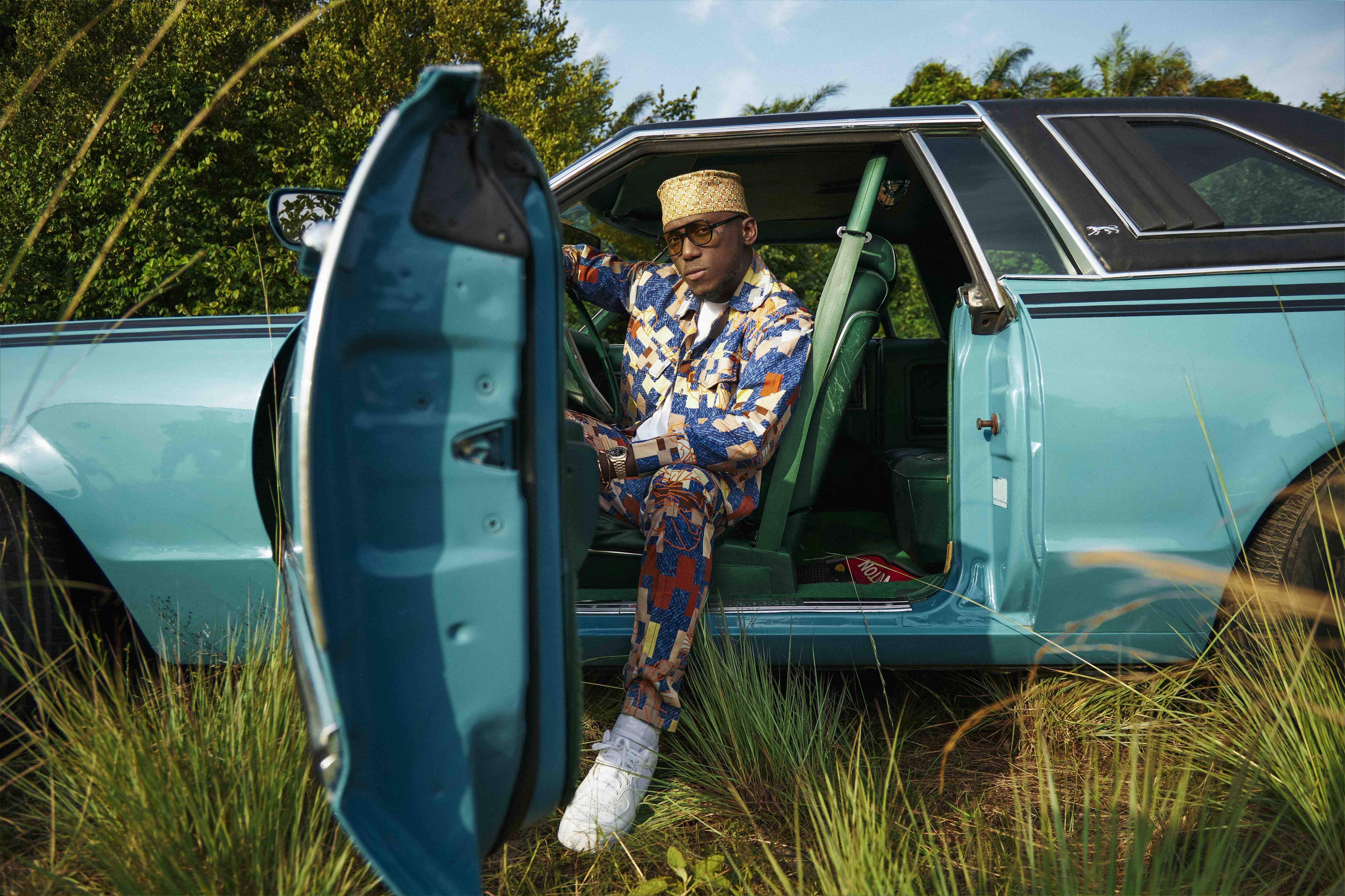 Spinall poses in a turquoise car parked in a grassy field